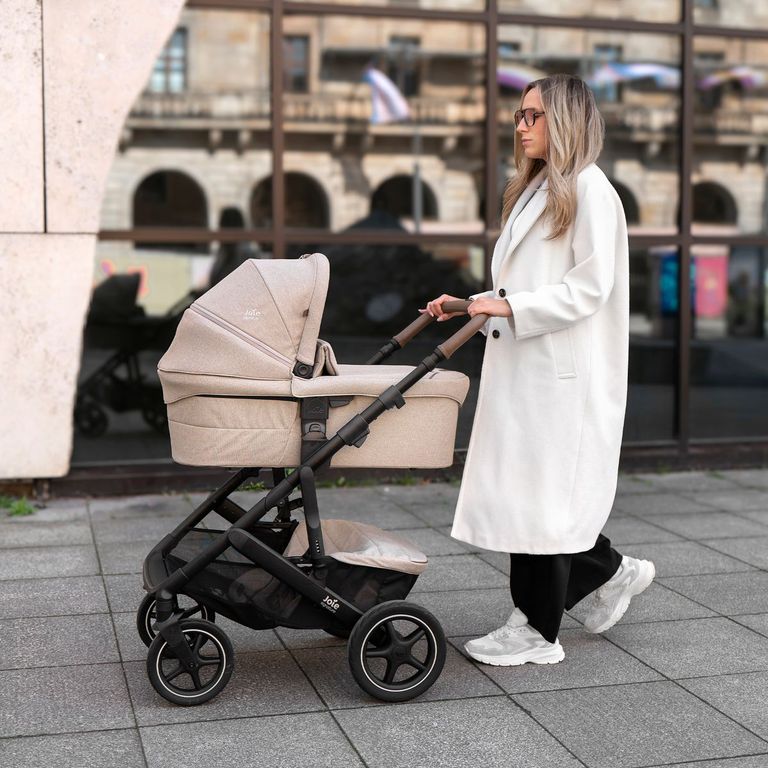 mutter mit weißem mantel schiebt joie signature kombi-kinderwagen vinca farbe sandstone