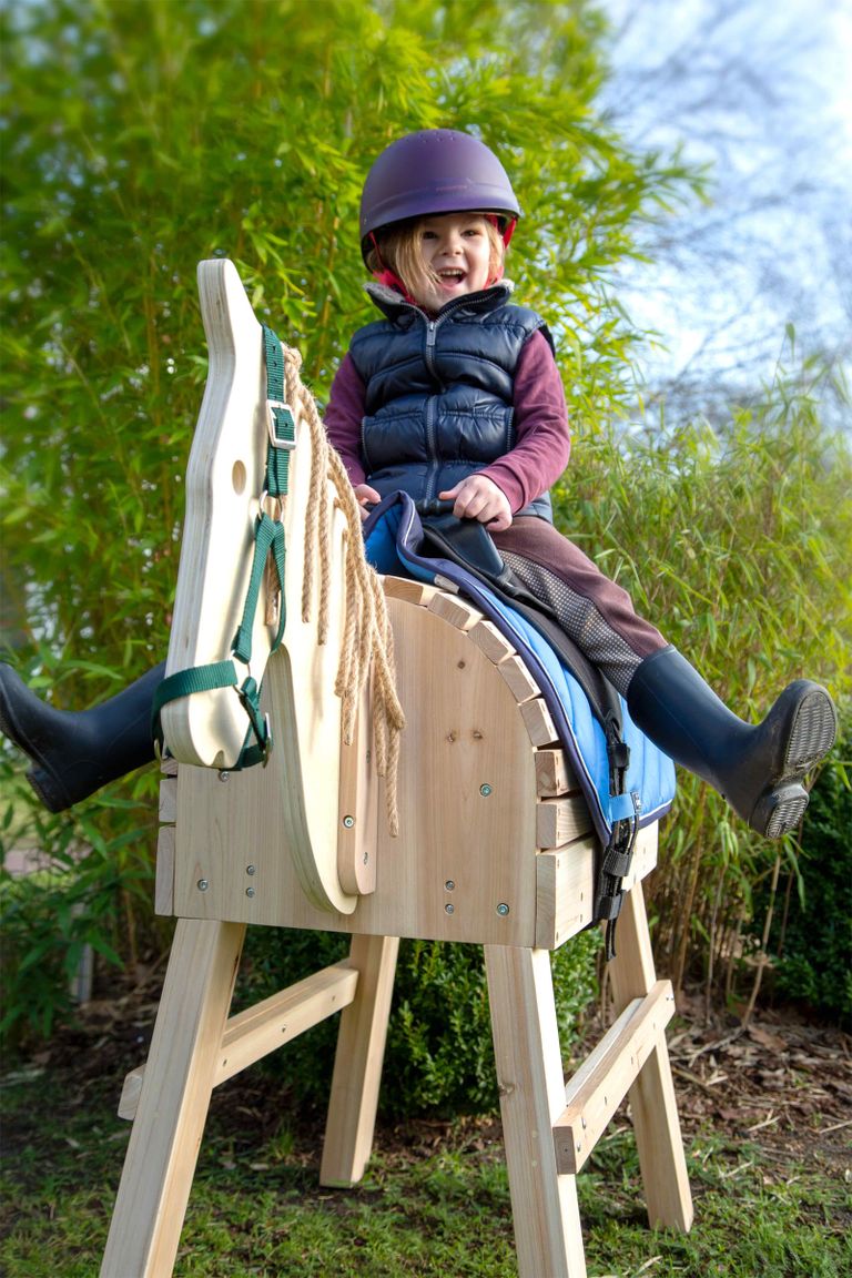 kind sitzt auf small foot holzpferd im garten