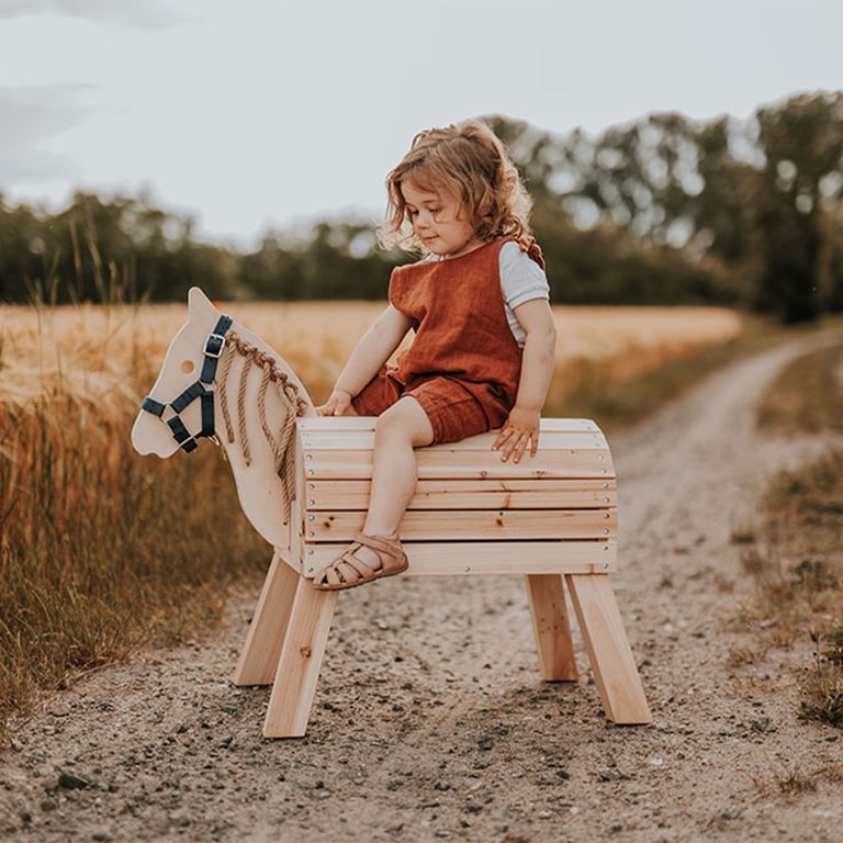kleines mädchen sitzt auf small foot holzpferd spielzeug für draußen